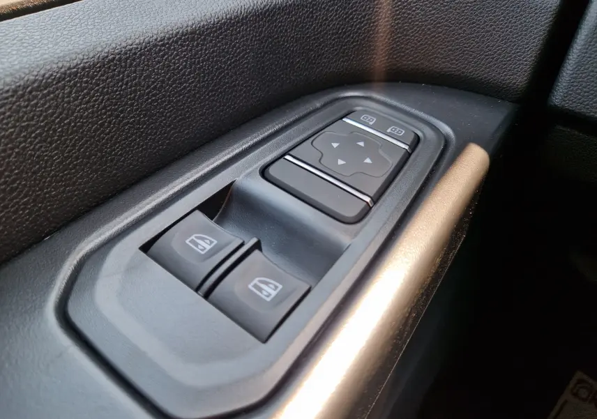Gros plan sur les commandes de lève-vitres et réglage des rétroviseurs côté conducteur du Renault Trafic Fourgon blanc 2026.