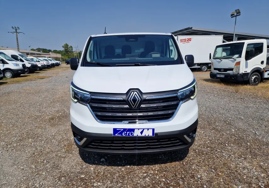 Renault Trafic Fourgon blanc en 3/4 avant droit, avec calandre noire et phares LED distinctifs, sur parking extérieur.