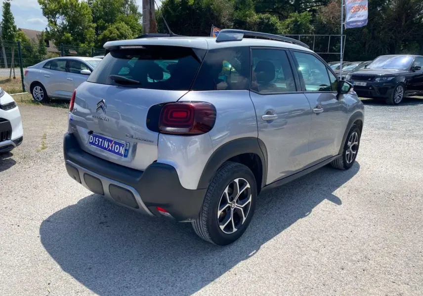 Vue 3/4 arrière droite d'un Citroën C3 Aircross gris Artense avec toit blanc, feux arrière distinctifs et jantes noires.