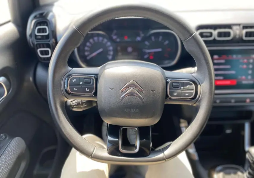 Vue rapprochée du volant noir de la Citroën C3 Aircross 2023, avec commandes intégrées et tableau de bord flou en arrière-plan.