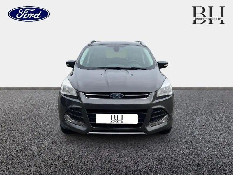 Vue frontale d'un Ford Kuga 2.0 TDCi Titanium gris Magnetic avec calandre chromée et phares halogènes allumés.
