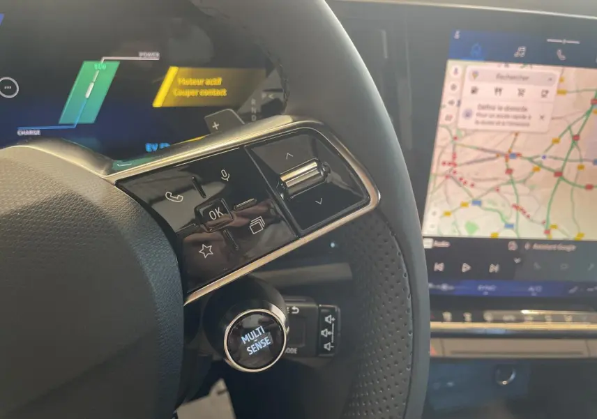 Gros plan sur le volant noir perforé du Renault Rafale 2025 avec bouton Multi-Sense et écran tactile de navigation visible.