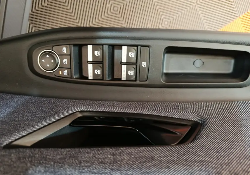 Gros plan sur les commandes de lève-vitres et rétroviseurs électriques sur la porte côté conducteur d'une Renault R5 blanche.