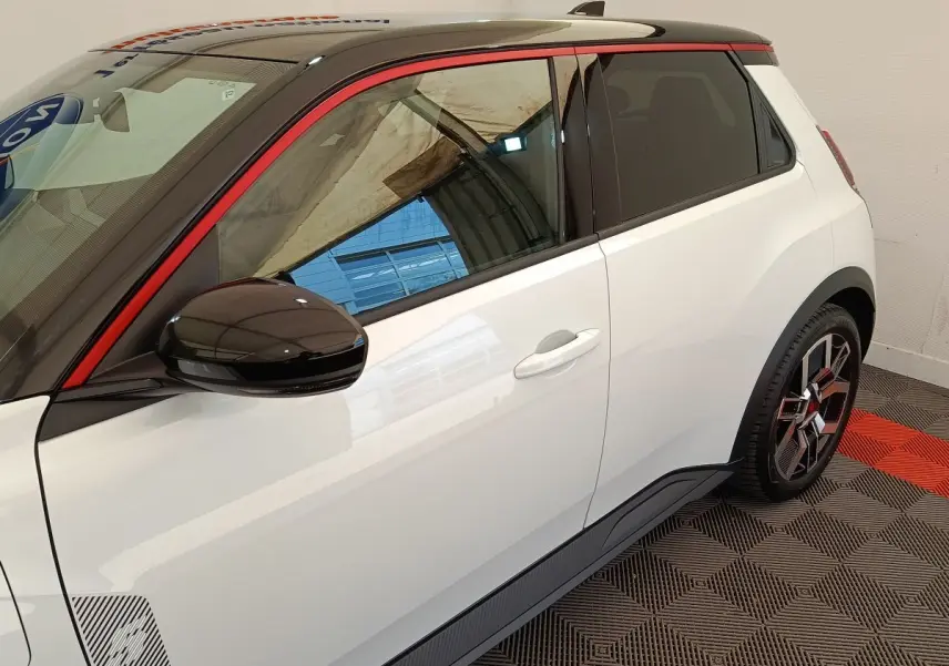 Vue côté droit arrière d'une Renault R5 Techno blanche avec toit noir, rétroviseur noir et jante stylisée rouge et noire.