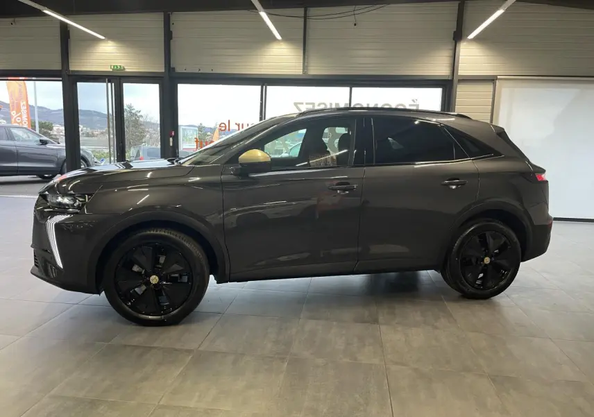 Vue latérale droite du DS7 Crossback gris titanium avec jantes noires et rétroviseurs dorés satinés en intérieur showroom.