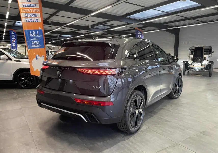 Vue 3/4 arrière droite du DS7 Crossback gris titanium avec feux arrière LED 3D et jantes alliage noires en showroom.