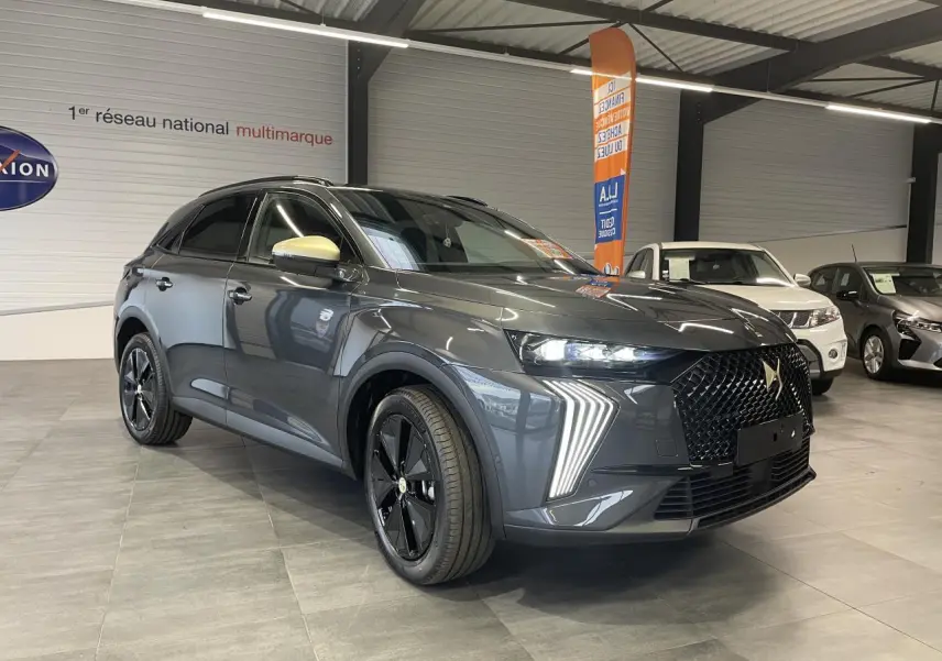 Vue 3/4 avant du DS7 Crossback gris titanium avec calandre noire et coques de rétroviseurs dorées satinées en showroom.