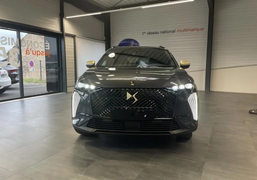 Vue frontale d'un DS7 Crossback gris titanium avec calandre noire brillante et feux LED verticaux allumés en showroom.
