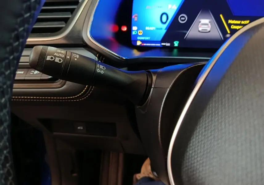Gros plan sur la manette de phares et clignotants à gauche du volant du Renault Symbioz bleu, tableau de bord numérique visible.
