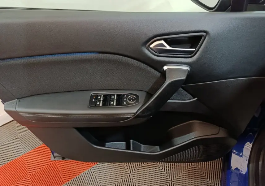 Vue intérieure côté gauche de la porte avant d’une Renault Symbioz bleu, avec commandes électriques et poignée noire.