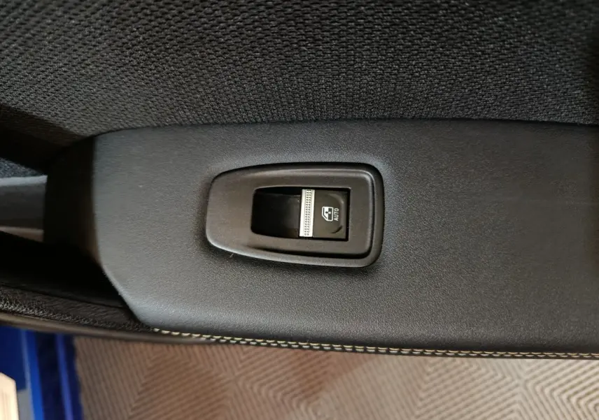 Gros plan sur l'interrupteur de lève-vitre électrique noir dans l'habitacle du Renault Symbioz bleu.