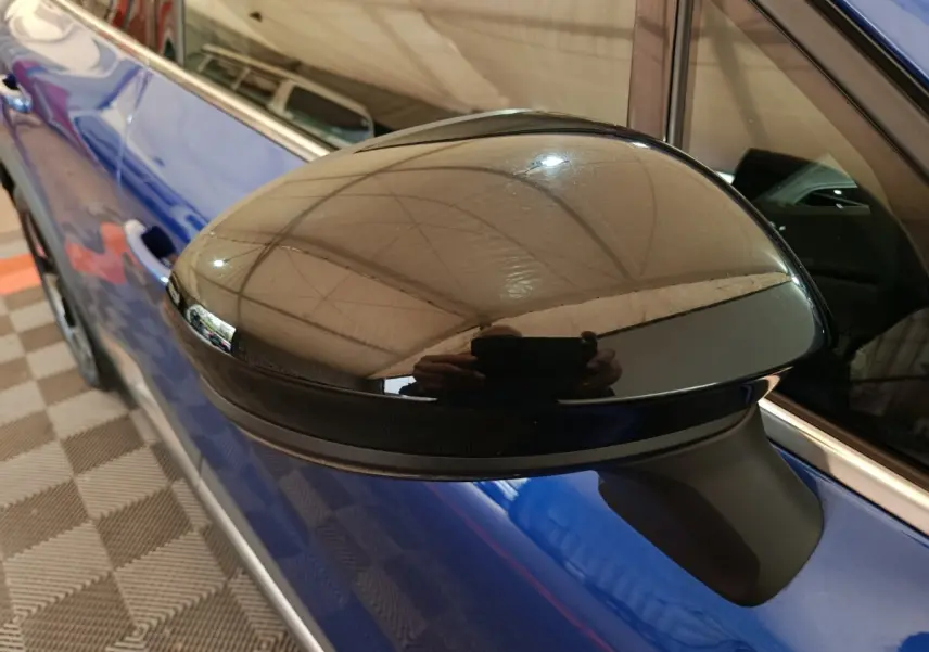 Gros plan sur le rétroviseur noir côté gauche d'une Renault Symbioz bleu électrique, avec reflet intérieur visible.