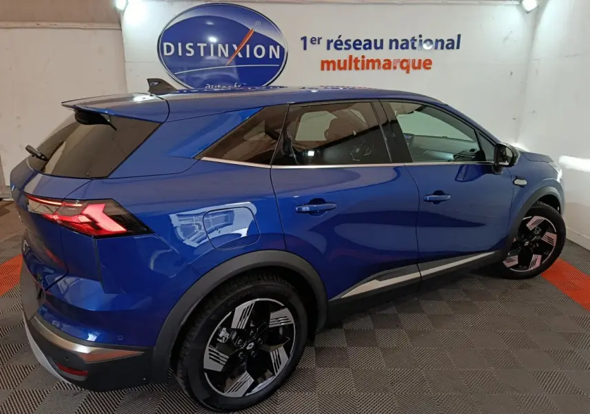 Vue 3/4 arrière droite d’un Renault Symbioz bleu électrique avec jantes noires et feux arrière LED allumés dans un showroom.