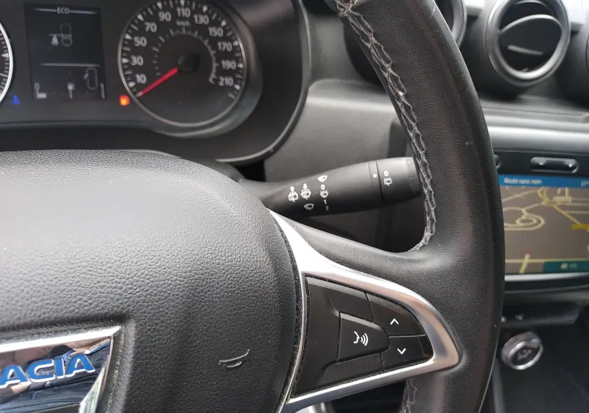 Gros plan sur le volant en cuir noir avec commandes intégrées du Dacia Duster 2020, tableau de bord et écran GPS visibles.