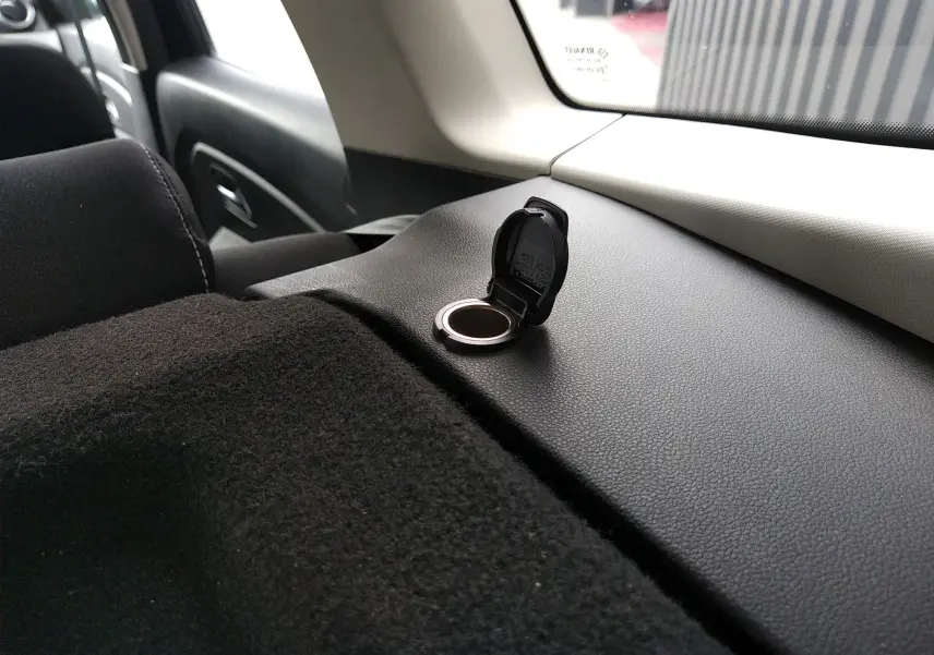 Détail de la prise 12V ouverte sur la plage arrière noire du Dacia Duster 1.5 DCI gris, vue intérieure côté gauche.
