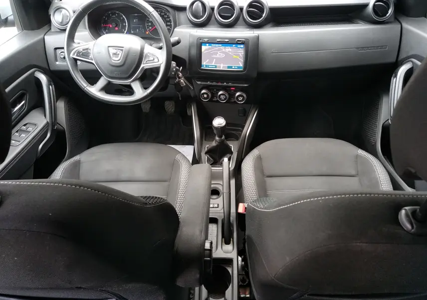 Vue intérieure avant du Dacia Duster gris 2020, avec tableau de bord, volant multifonction et écran tactile GPS.