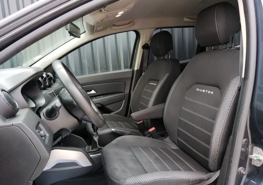 Vue intérieure côté conducteur du Dacia Duster gris 2020, sièges noirs avec logo Duster brodé et volant cuir.