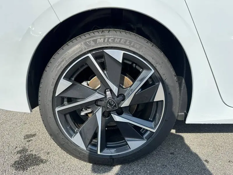Gros plan sur la roue avant droite d'une Peugeot 308 2025 blanche avec jante alliage noire et grise au design géométrique.