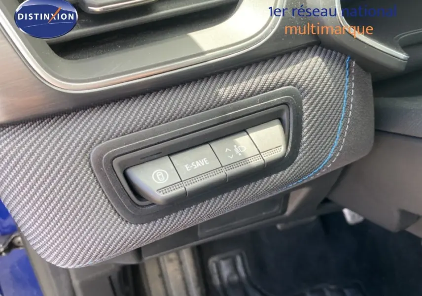 Gros plan sur les commandes E-SAVE et réglage des phares sur la planche de bord en tissu carbone bleu du Renault Symbioz 2025.