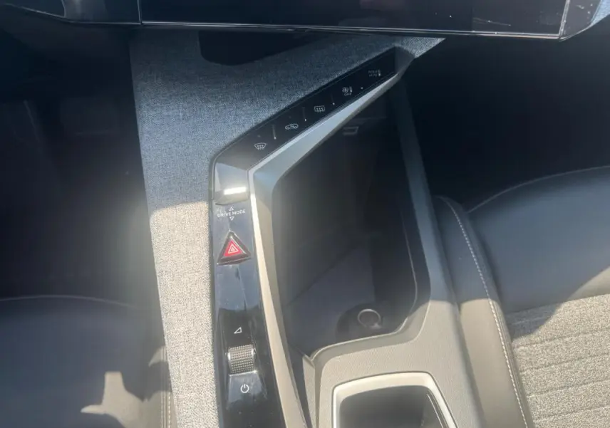 Vue plongeante sur la console centrale grise du Peugeot 5008 Hybrid 2025 avec commandes tactiles et rangement intégré.