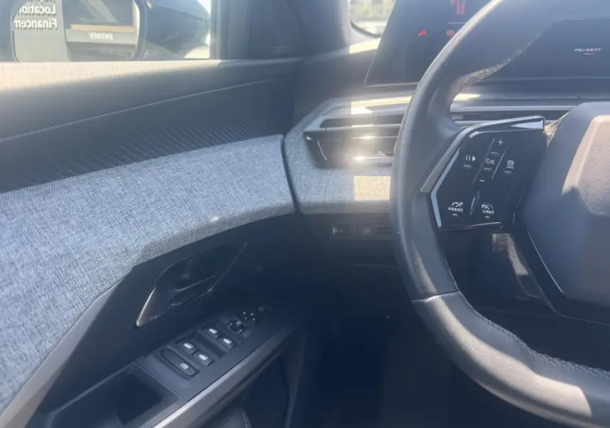 Intérieur du Peugeot 5008 Hybrid 2025, vue côté conducteur sur volant, commandes et panneau de porte gris clair.