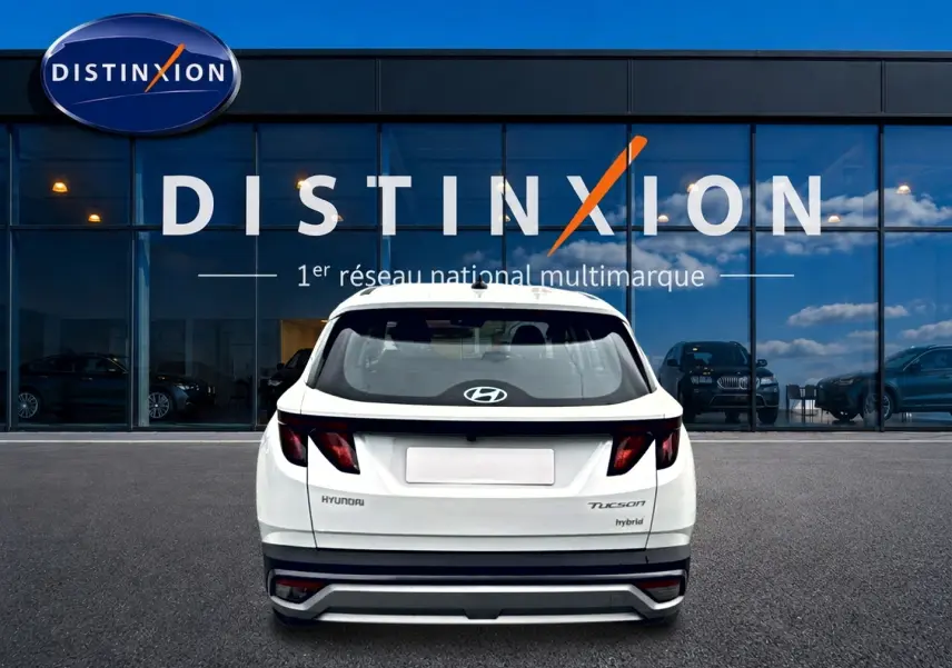 Vue arrière d'un Hyundai Tucson blanc hybride 2026 garé devant une vitrine avec logo Distinxion.