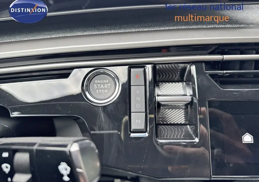 Gros plan sur la console centrale noire brillante du Peugeot 3008 Hybrid 2025 avec bouton start/stop et commandes de boîte auto.