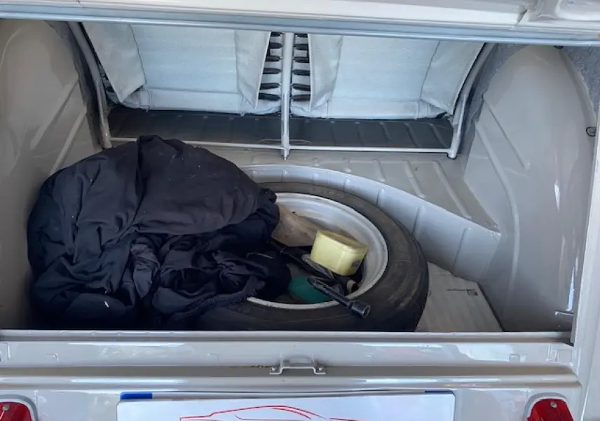 Coffre ouvert d'une Citroën 2 CV beige clair refaite à neuf, montrant une roue de secours et des objets à l'intérieur.