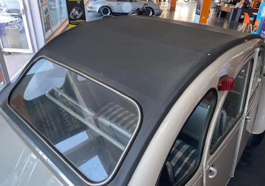 Vue 3/4 arrière droite d'une Citroën 2 CV beige clair de 1968 rénovée, avec toit ouvrant en toile noire et feux arrière rouges.