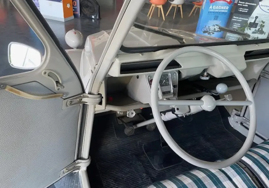 Vue intérieure côté gauche de la Citroën 2 CV beige clair de 1968, volant fin et tableau de bord minimaliste.