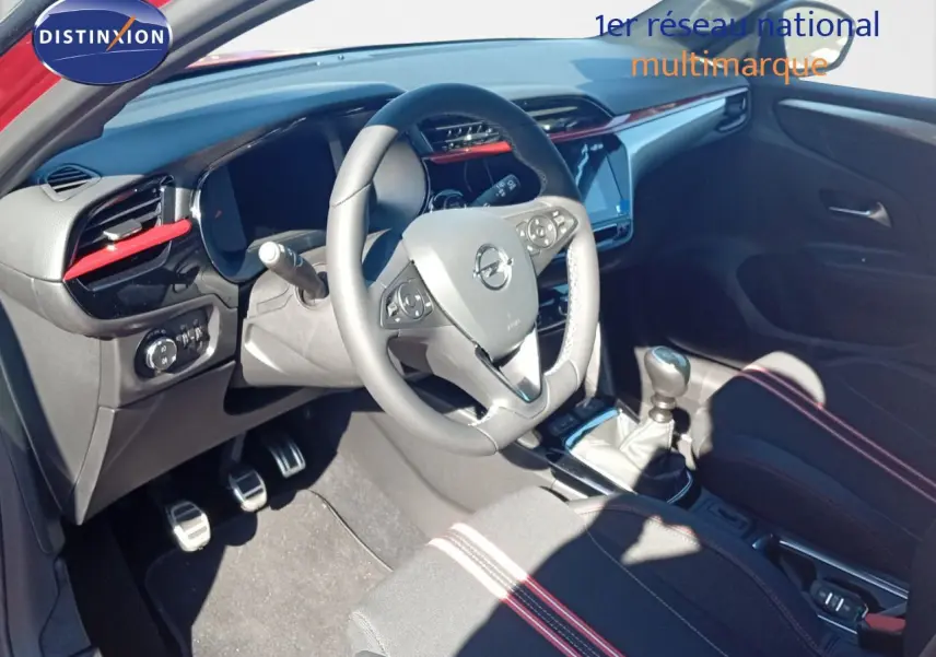 Intérieur avant droit d'une Opel Corsa rouge avec volant multifonction, levier de vitesse manuel et détails rouges sur tableau de bord.