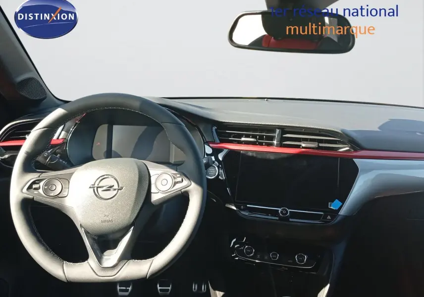 Vue intérieure centrée sur le volant et tableau de bord noir avec bande rouge de l'Opel Corsa rouge 2023.