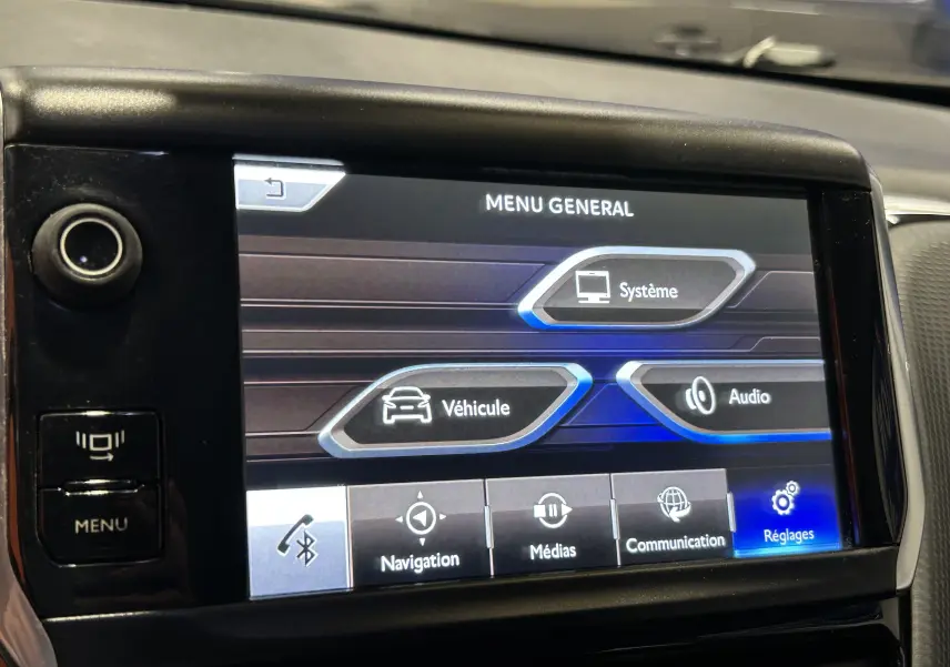 Écran tactile central du tableau de bord du Peugeot 2008 blanc, affichant le menu général avec options système, véhicule et audio.