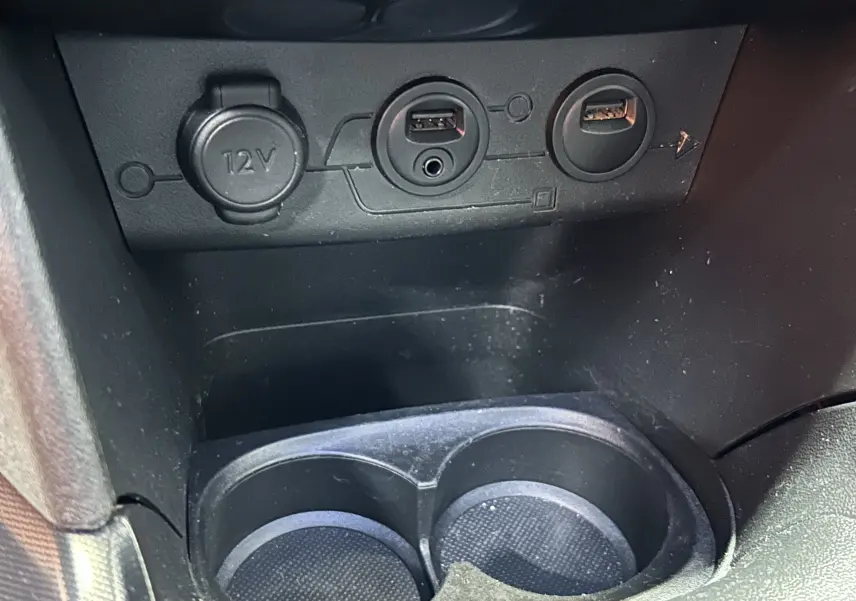 Gros plan sur la console centrale d'une Peugeot 2008 blanche, montrant prises USB, prise 12V et porte-gobelets.