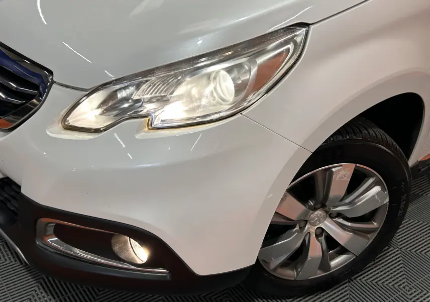 Gros plan sur l'avant droit blanc du Peugeot 2008 VTi 82 Allure avec phare et antibrouillard allumés.