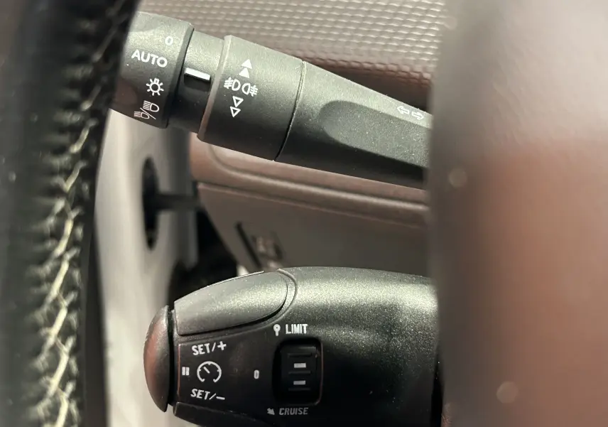 Gros plan sur les commandes de régulateur de vitesse et des feux sur le volant d’un Peugeot 2008 blanc de 2014.