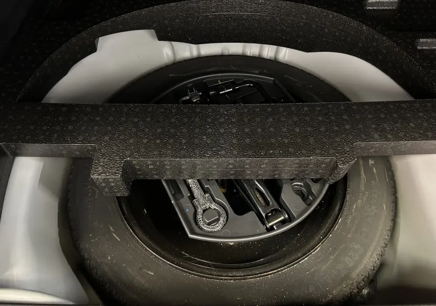 Vue rapprochée de la roue de secours noire et de ses outils dans le coffre d’un Peugeot 2008 blanc de 2014.