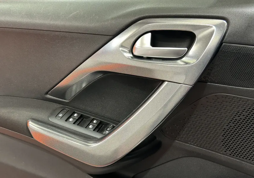 Vue rapprochée de la poignée intérieure côté gauche de la porte avant d'une Peugeot 2008 blanche, avec commandes de vitres.