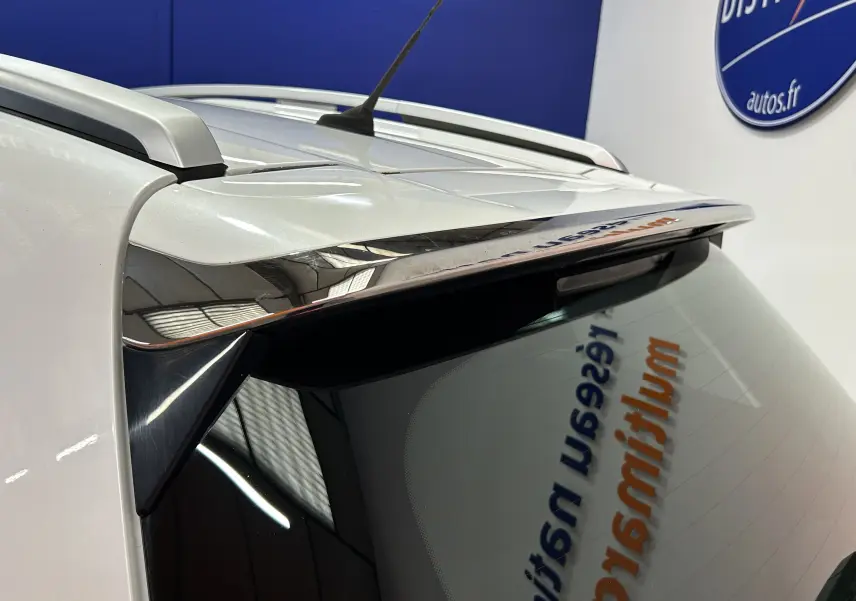 Gros plan sur l'angle arrière droit d'une Peugeot 2008 blanche, mettant en valeur l'aileron et la lunette arrière teintée.