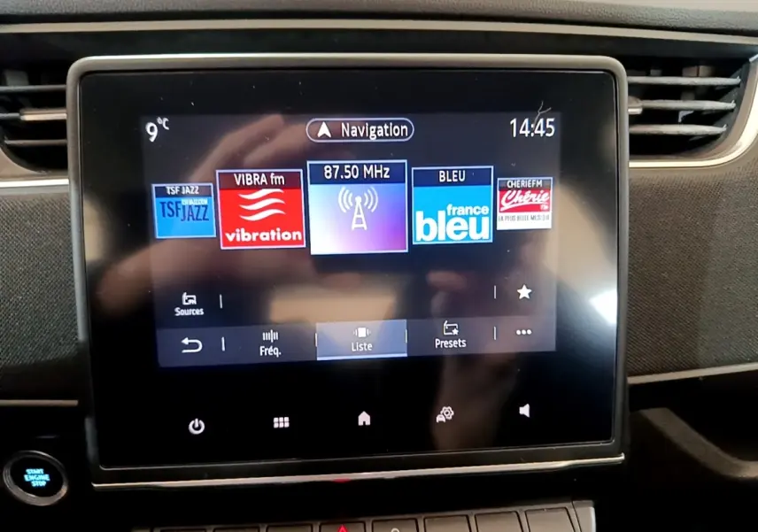 Écran tactile central de la Renault ZOE Business R110 blanc, affichant les stations radio avec bouton démarrage visible à gauche.