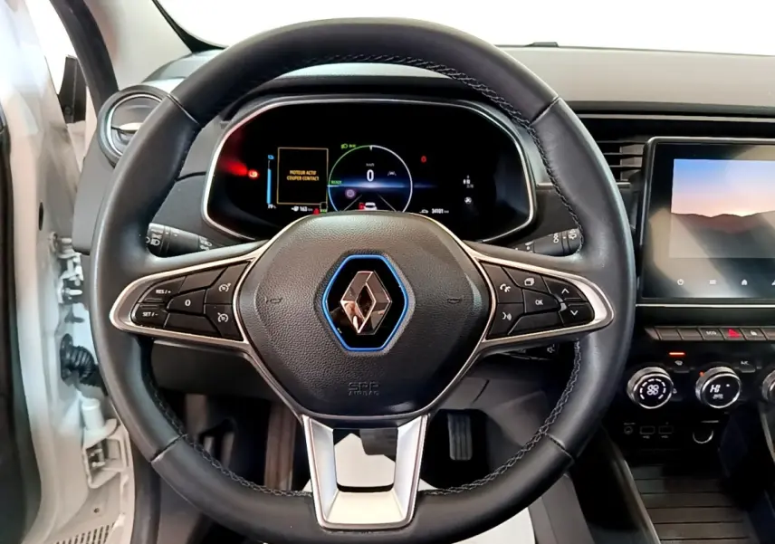 Vue intérieure centrée sur le volant cuir noir de la Renault ZOE blanc, avec tableau de bord digital et écran tactile visible.