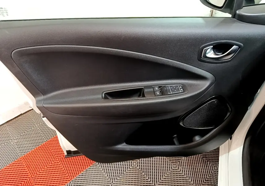 Vue rapprochée de la porte avant gauche noire de la Renault ZOE Business R110 blanche, avec commandes de vitres et haut-parleur intégré.