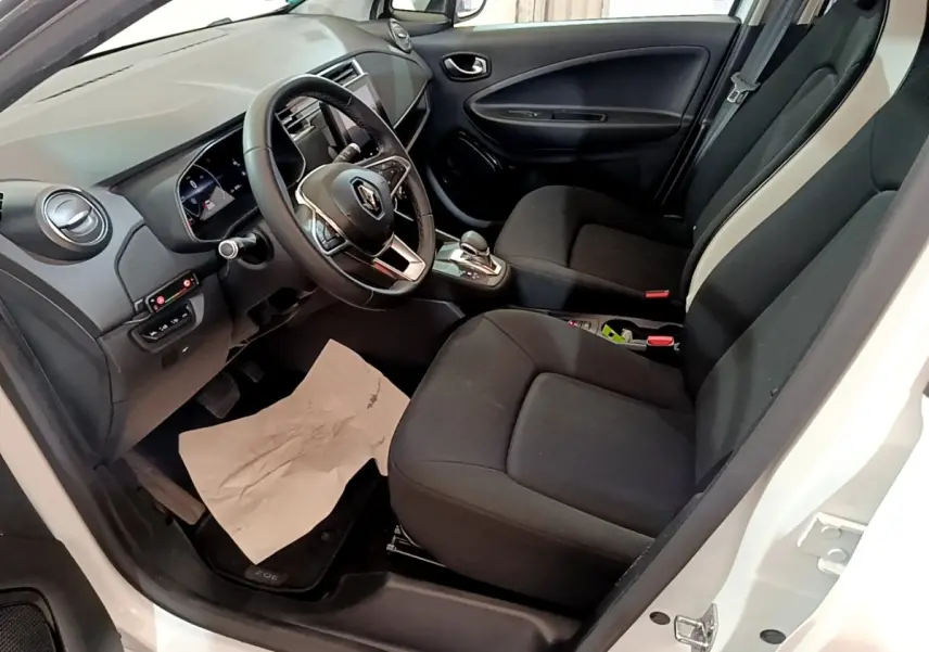 Vue intérieure côté conducteur de la Renault ZOE Business R110 blanc, avec volant multifonctions et sièges noirs.