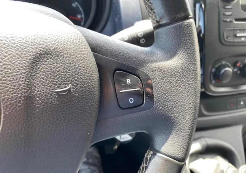 Gros plan sur le volant en cuir noir de l'Opel Vivaro blanc, avec commandes intégrées visibles à droite.