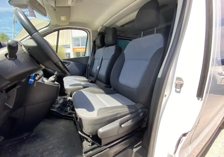 Vue intérieure côté conducteur de l'Opel Vivaro blanc 2018, montrant les sièges avant en tissu gris et noir.
