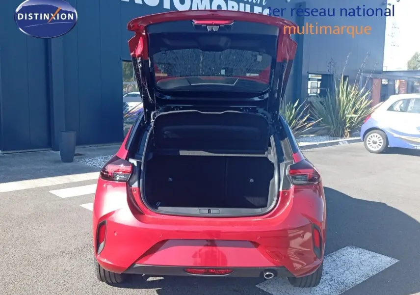 Vue arrière d'une Opel Corsa rouge Kardio métal avec toit noir, coffre ouvert en extérieur sur parking.