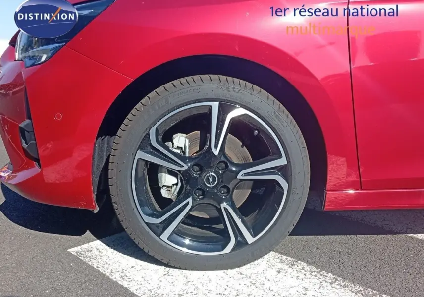 Gros plan sur la roue avant gauche d'une Opel Corsa rouge Kardio métal avec jante noire et détails argentés.