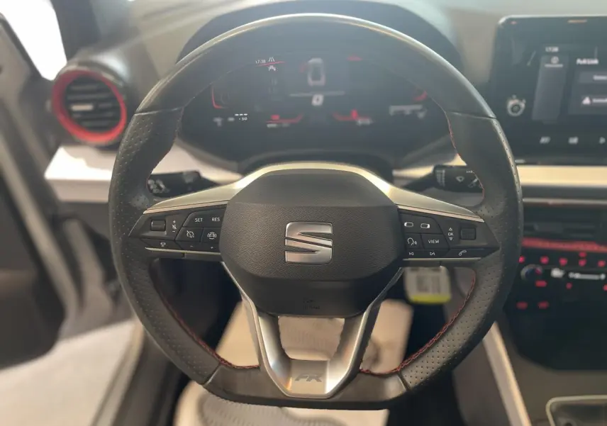 Vue rapprochée du volant sport cuir noir avec surpiqûres rouges du SEAT Arona FR 2024, tableau de bord digital en arrière-plan.