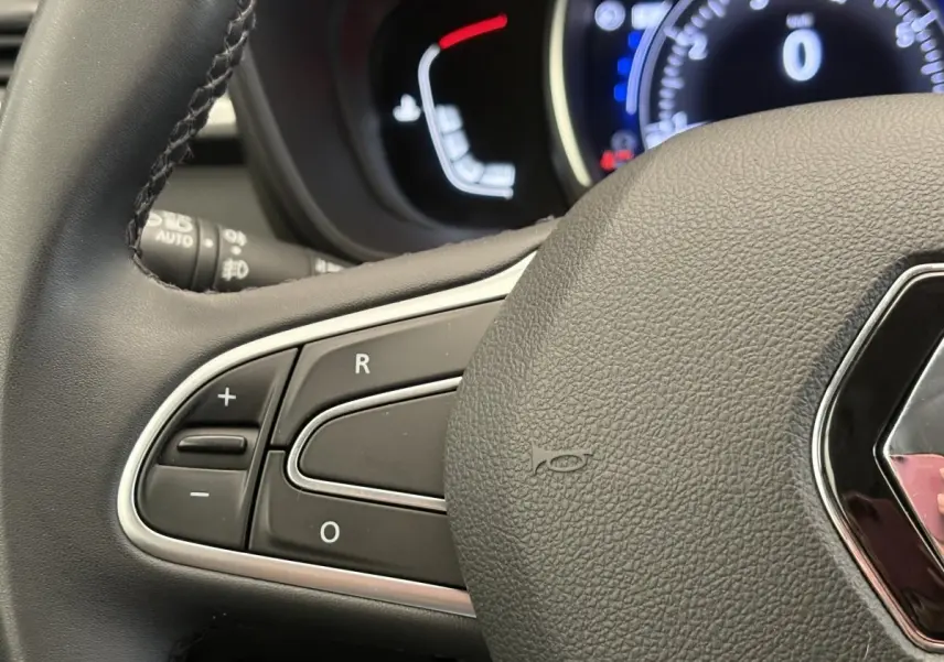 Gros plan sur le volant cuir gris foncé de la Renault Kadjar avec commandes intégrées et tableau de bord lumineux en arrière-plan.