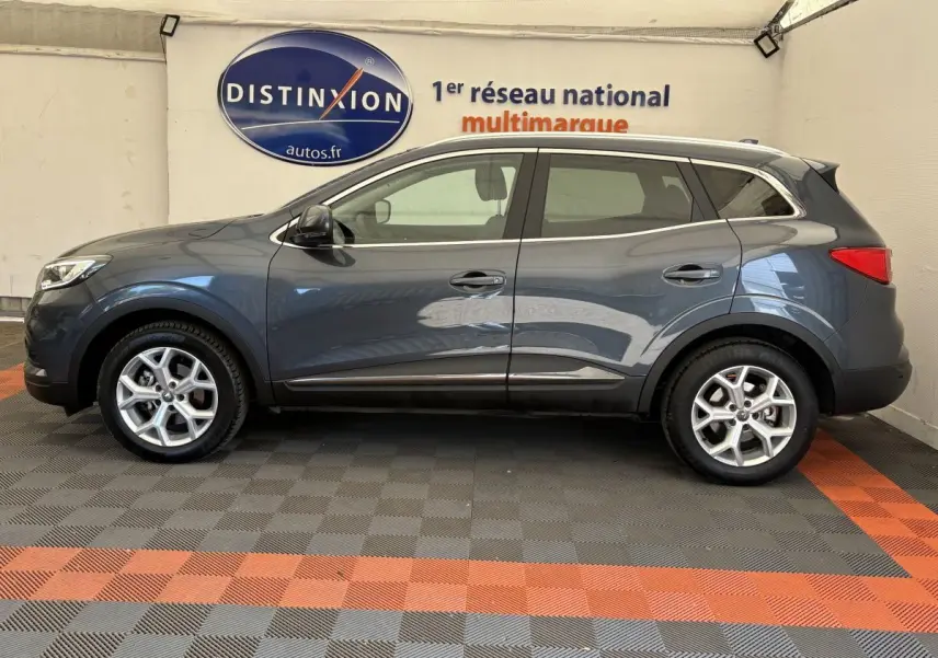 Profil droit d’un Renault Kadjar gris foncé 2019 garé en intérieur avec jantes alliage et barres de toit chromées.